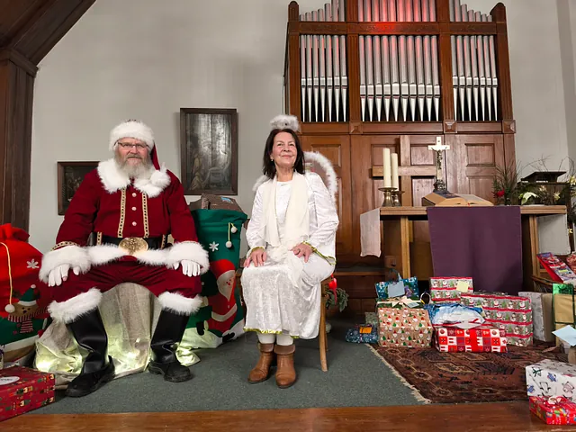 Zwei Kinder mit Wintermützen und Schals reichen sich ein Geschenk mit grünem Schleifenband