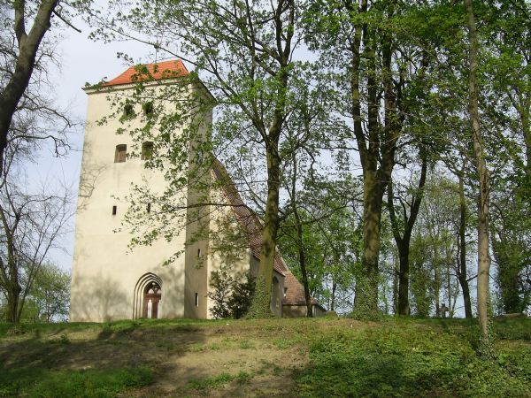 Weißer Turm der Kirche in Booßen mit rotem Dach hinter Bäumen auf einem grasbewachsenen Hügel