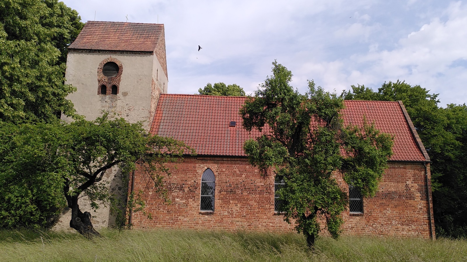 Alte Backsteinkirche mit rotem Ziegeldach und zwei Bäumen im Vordergrund