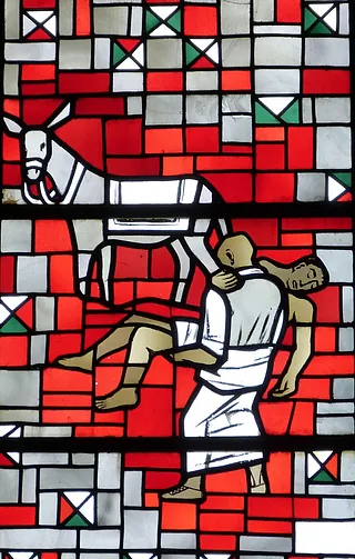 Buntes Kirchenfenster mit der Darstellung eines Mannes, der einen bewusstlosen anderen Mann trägt.