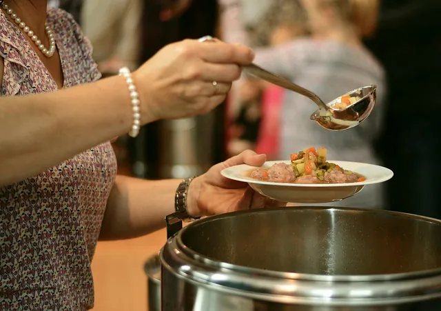 Frau mit Perlenarmband schöpft mit einer Kelle Essen auf einen Teller