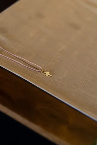 Goldener Kreuzanhänger an einer dünnen Kette auf einem beigen Stoff liegend